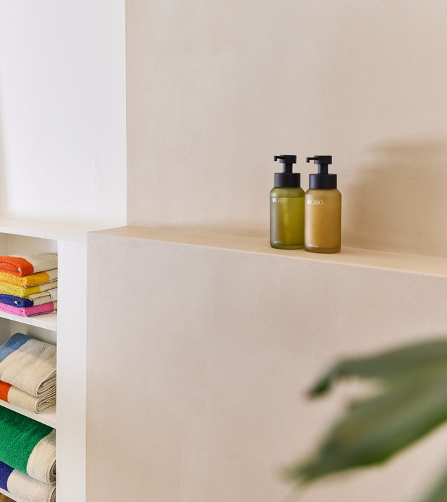 Mortex wand in badkamer met kleurrijke handdoeken en twee stijlvolle zeepdispensers op een nisplank.