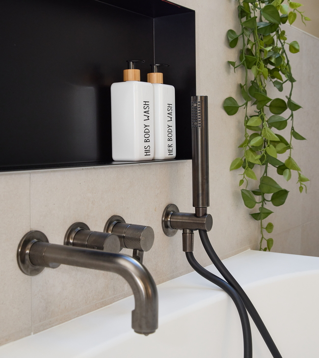 Detail van een modern bad met zwarte kranen en nismuur in een stijlvolle en vernieuwde badkamer met groene accenten.
