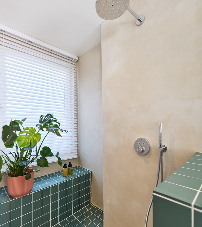 Regendouche met inbouwkraan, mortex wanden en groene tegels in moderne douche met planten en natuurlijke lichtinval.