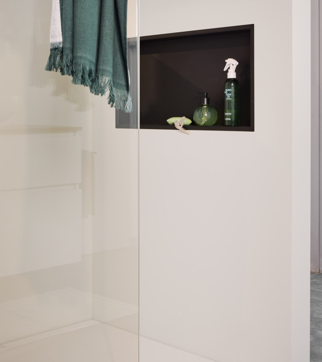 Witte inloopdouche met helder glas en een zwarte inbouwnis met badartiklen